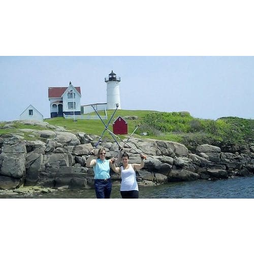 Two Women Holding Up Walking Poles Posing in Front of a Lighthouse