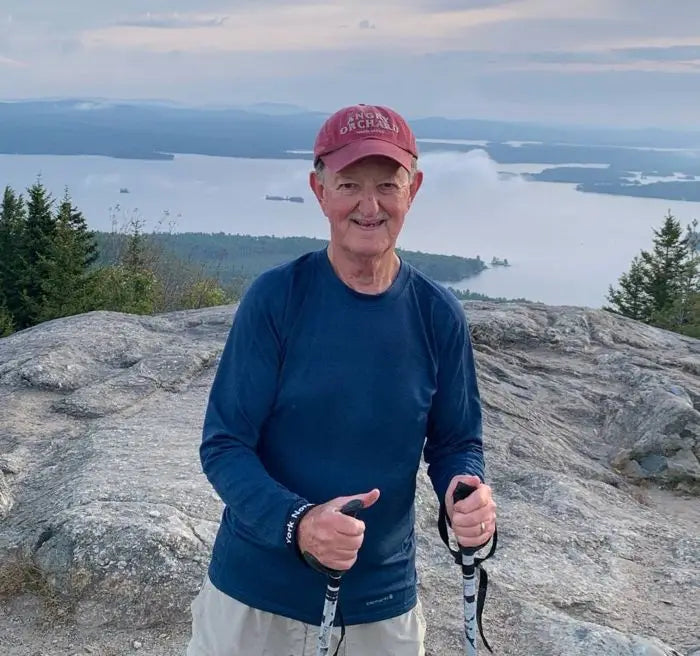 Man with walking poles at top of a mountain with a lake in the background